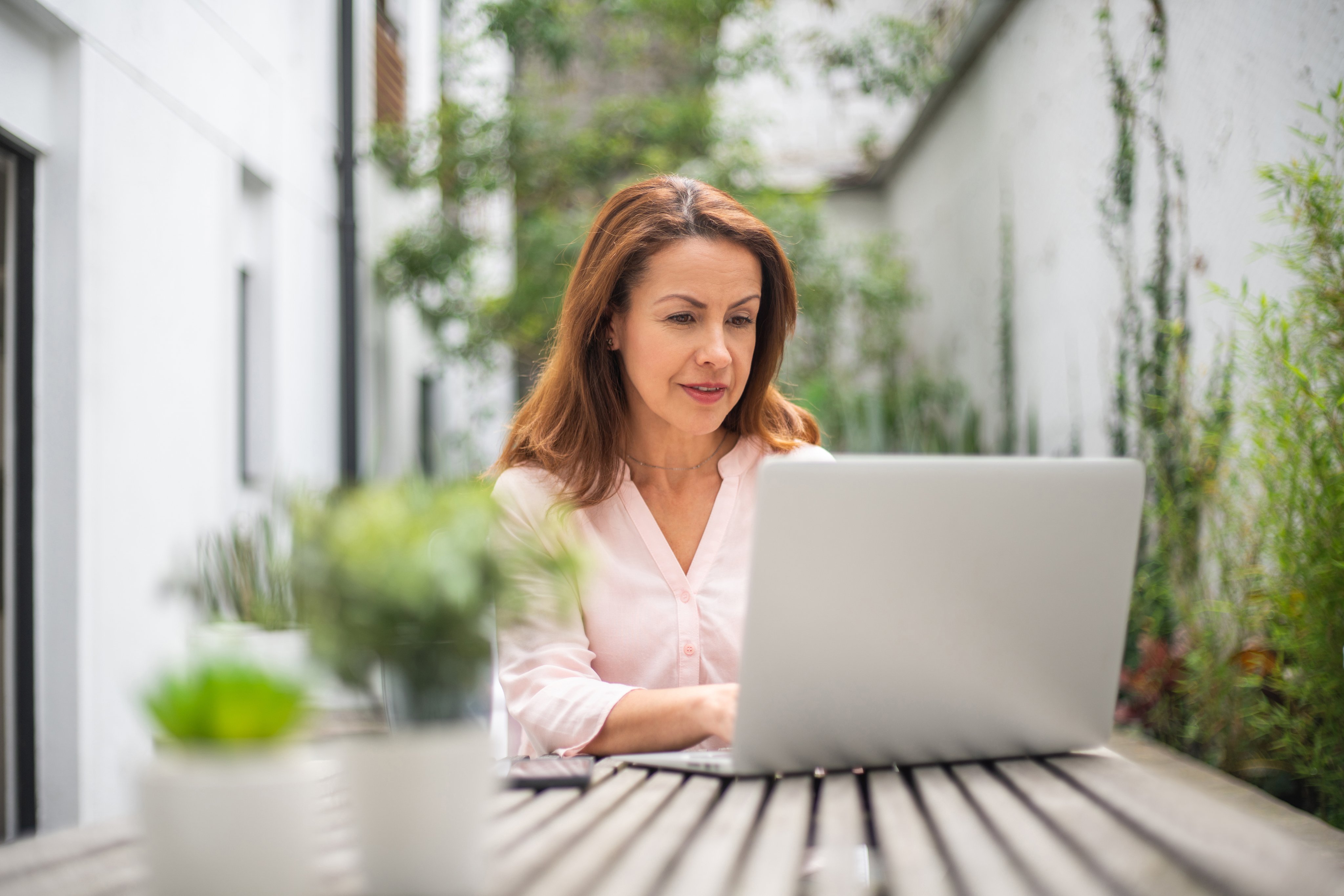 Woman working through an online course on her laptop at an outdoor courtyard table.