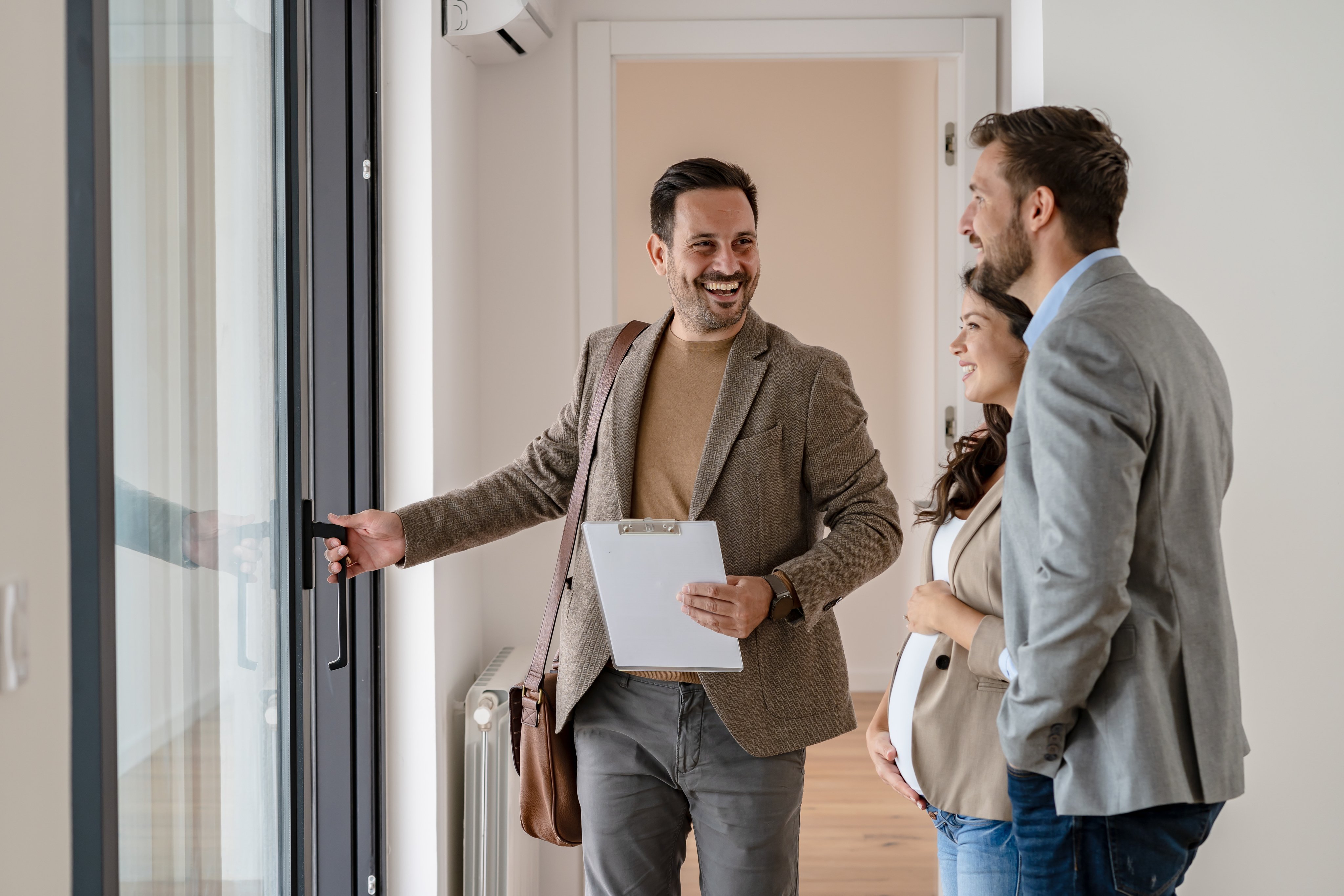 A real estate agent welcoming a couple at the doorway of a modern home for a viewing.