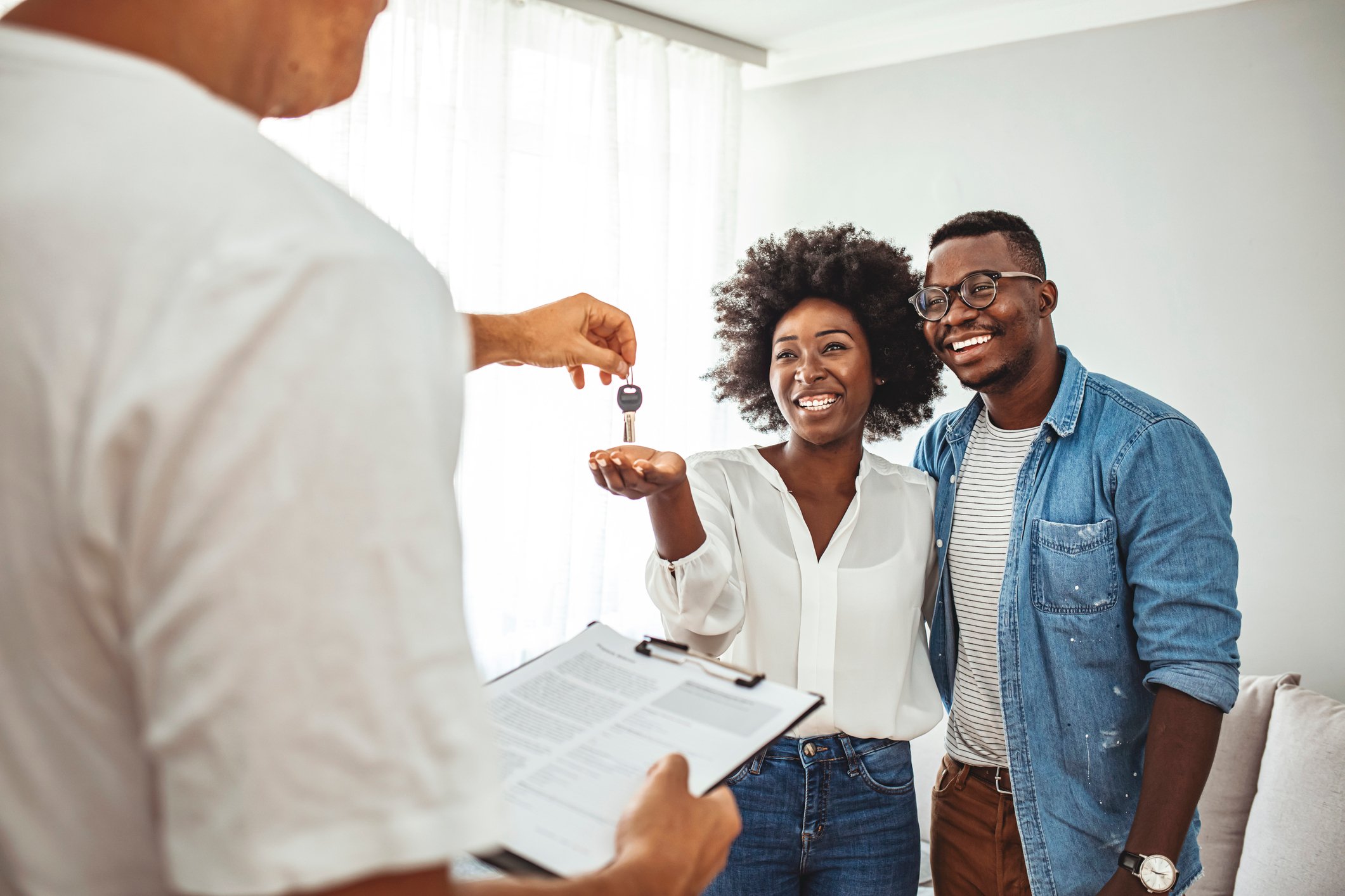 Real estate agent handing house keys to a happy young couple in their new home.