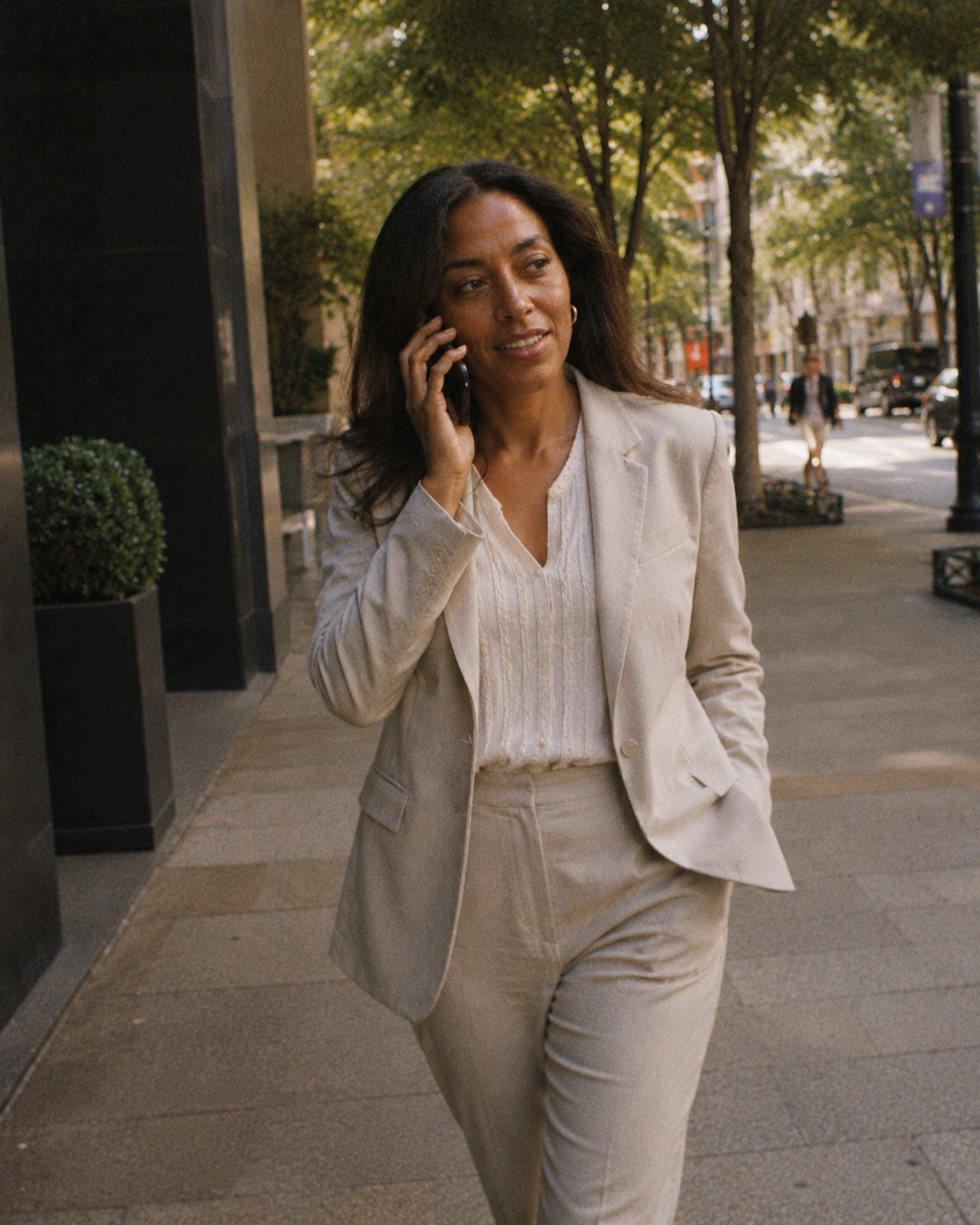 A professional walks down a city street speaking on a mobile phone, mid-conversation.