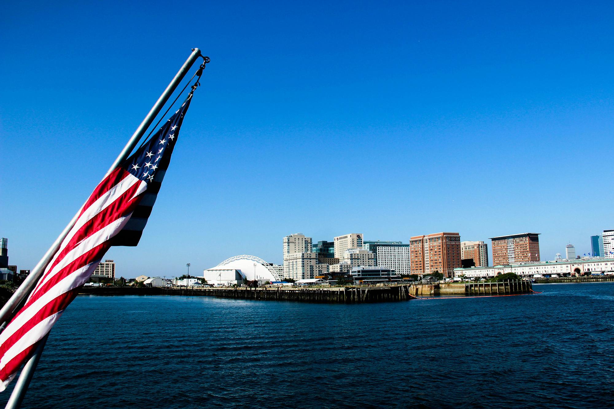 American flag over a harbor with city skyline