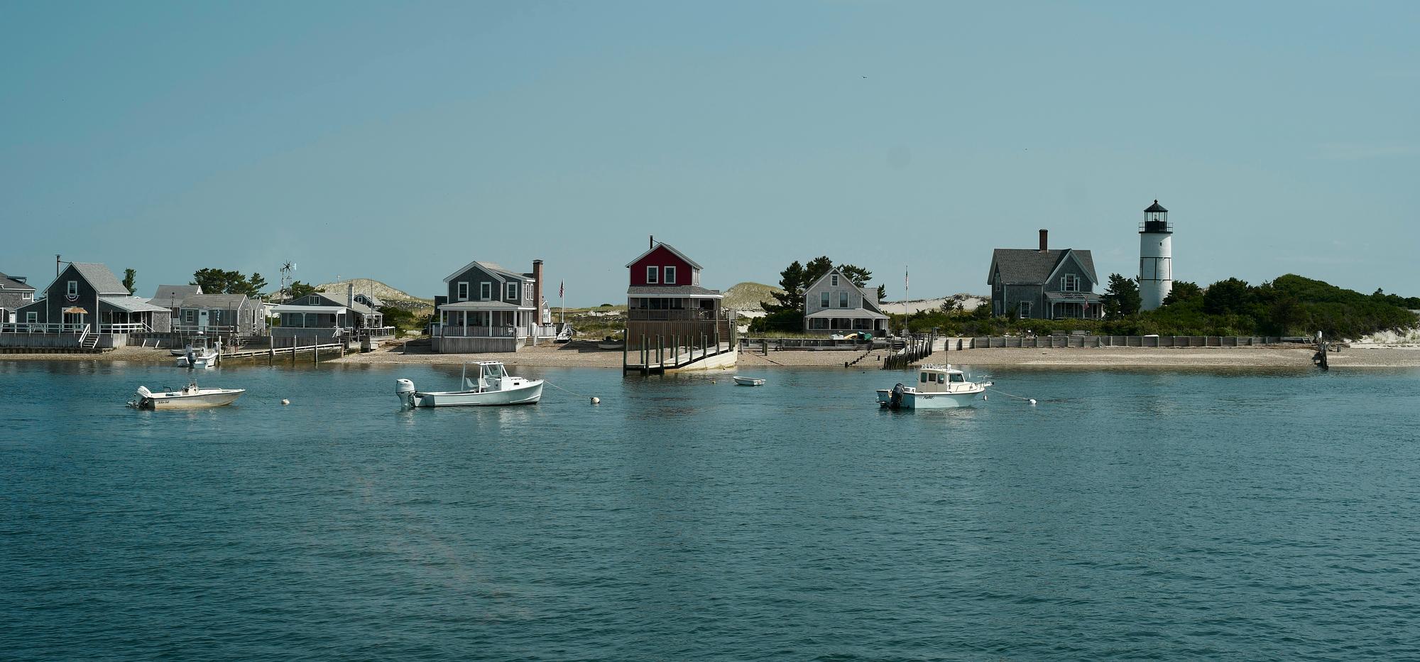 Sailboats and a lighthouse in a New England harbor at golden hour