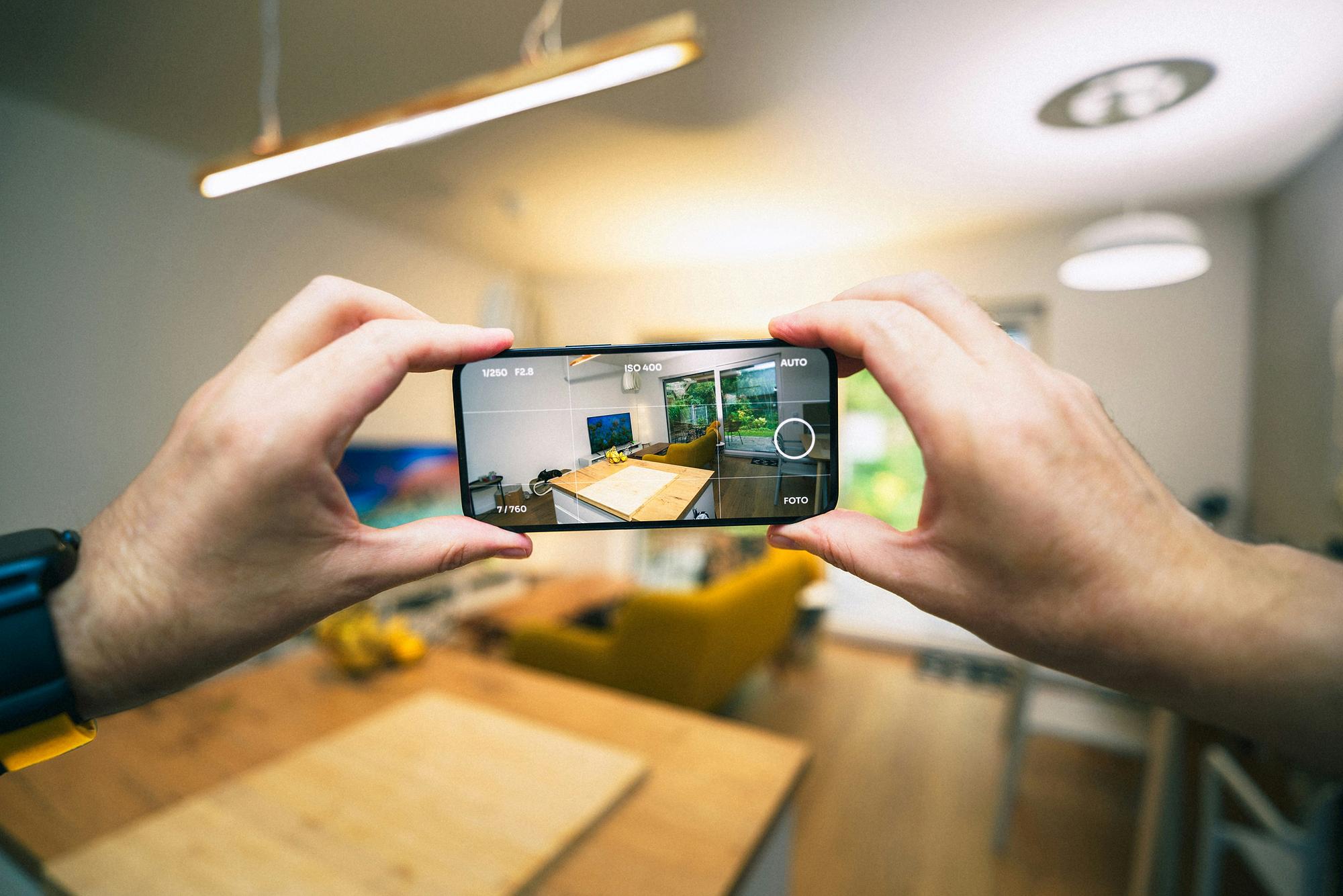 Hands holding a smartphone to photograph a home's kitchen and living area, the kind of interior photos an appraisal report includes.