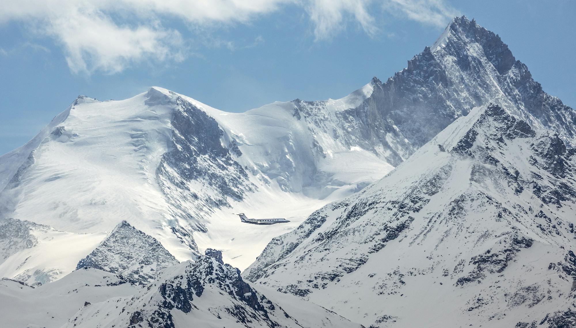 Private jet flying past snowy peaks toward mountain airports in winter